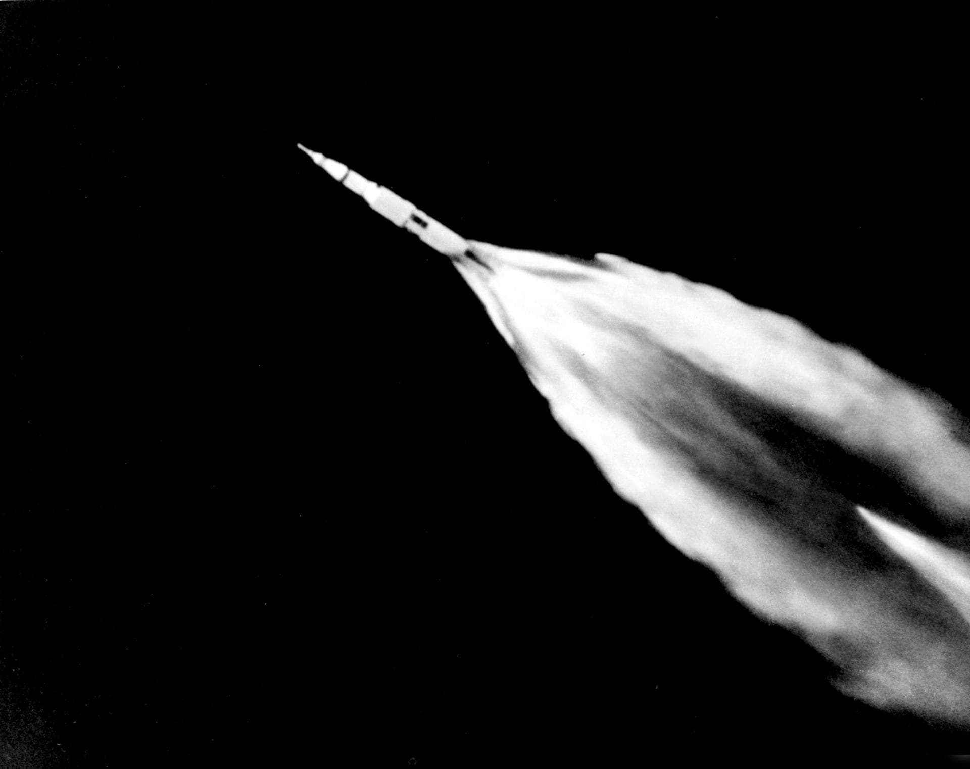 Black-and-white photo of the Apollo 11 Saturn V rocket climbing with a long plume.