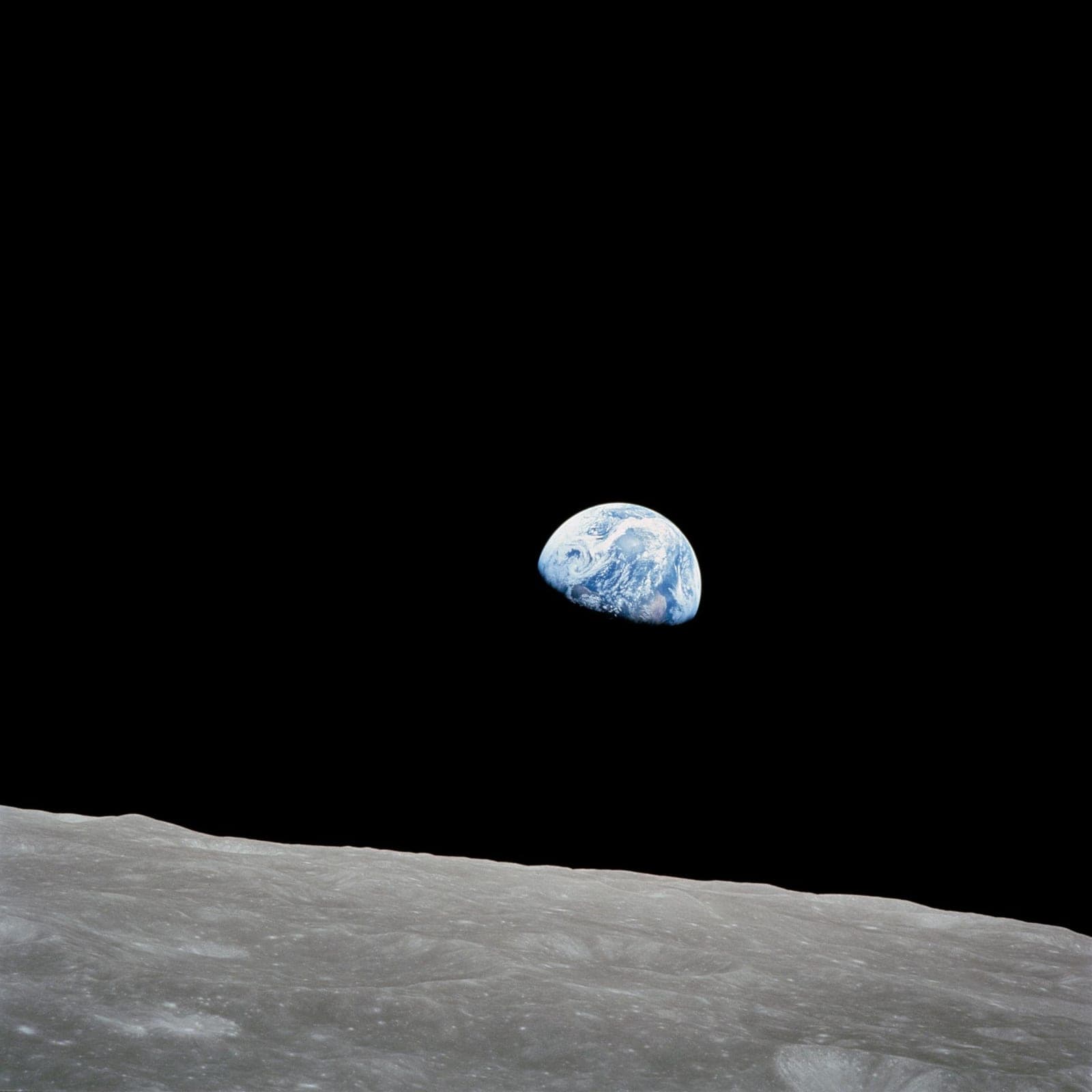 Half-lit blue Earth rising above the grey, cratered horizon of the Moon.