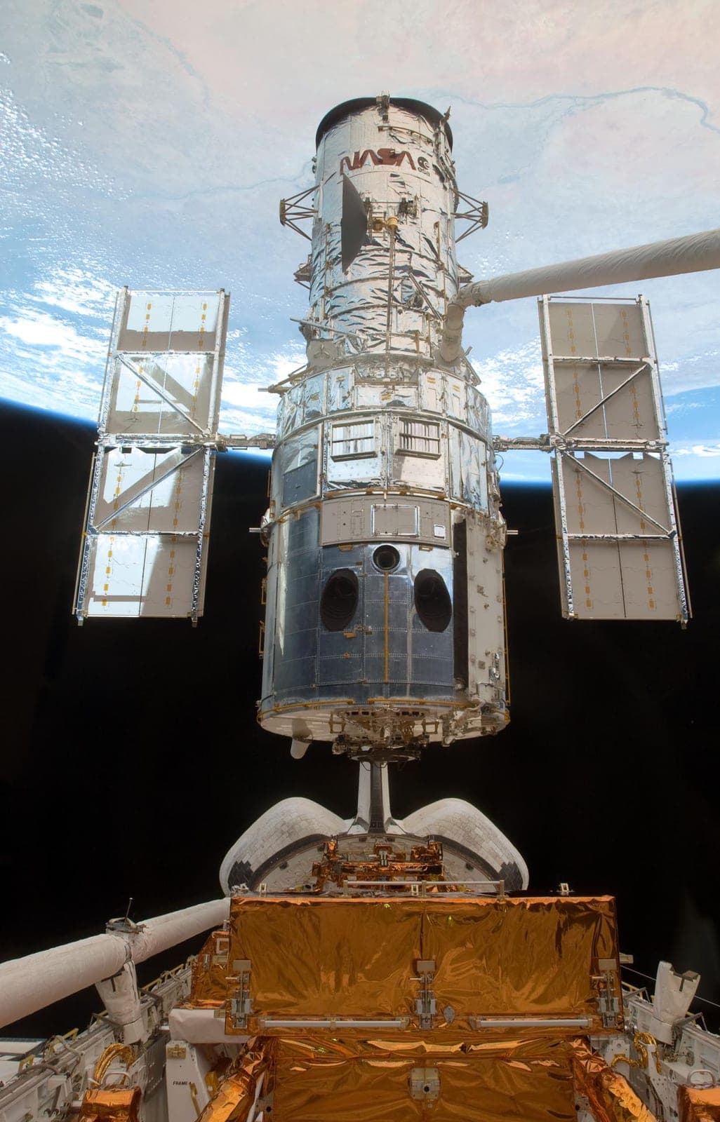 The Hubble Space Telescope with open solar panels above the shuttle's cargo bay, Earth behind it.