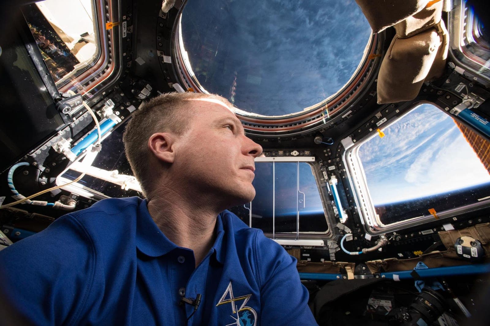 An astronaut looking out of the round windows of the Cupola, with Earth beyond them.