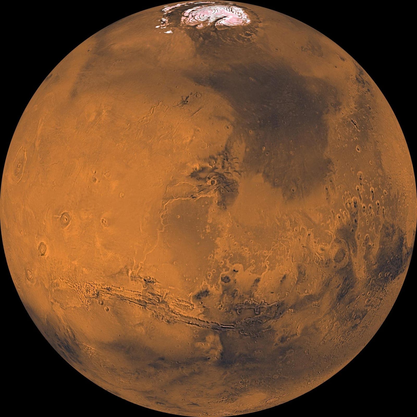 Rust-colored globe of Mars with a white polar cap and a long canyon across its middle.