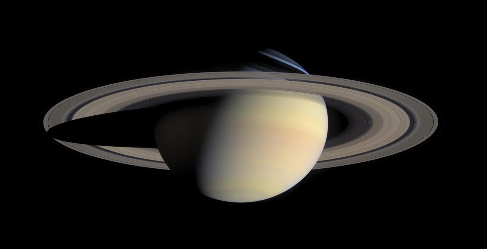 Saturn in pale gold with its wide rings, the planet casting a shadow across them.