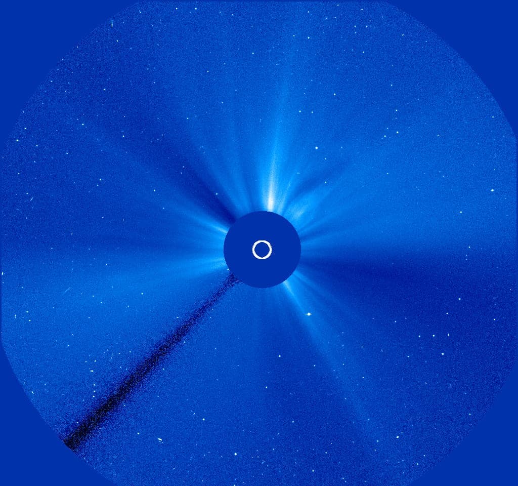 A blue field with bright streamers around a dark disk in the middle and scattered stars.